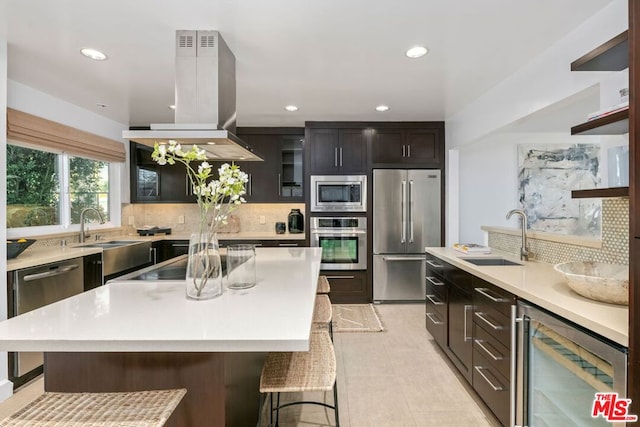 kitchen featuring sink, a breakfast bar, appliances with stainless steel finishes, a center island, and island exhaust hood