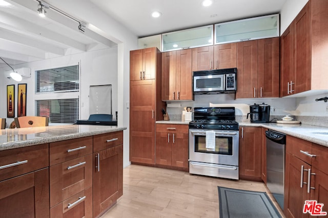 kitchen with appliances with stainless steel finishes, beam ceiling, light stone countertops, and light hardwood / wood-style floors