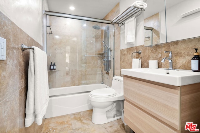 full bathroom with combined bath / shower with glass door, tile walls, tile patterned flooring, vanity, and toilet