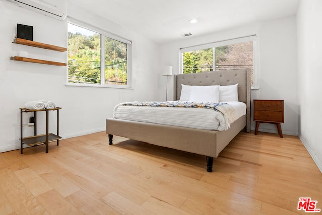 bedroom with a wall unit AC and light hardwood / wood-style floors