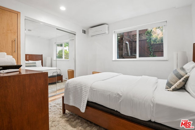 bedroom with a wall mounted AC, a closet, and light wood-type flooring