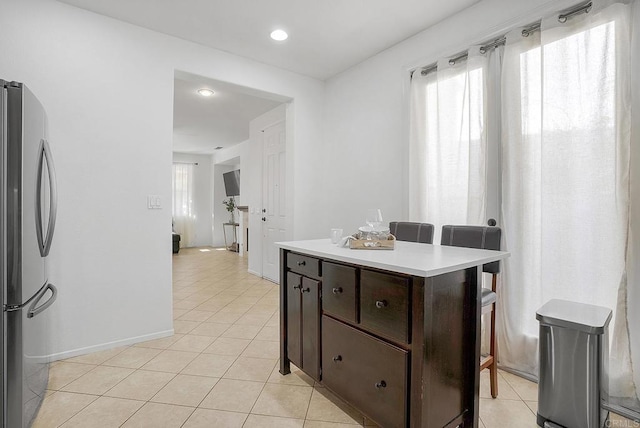 kitchen with dark brown cabinets, light tile patterned floors, and stainless steel refrigerator