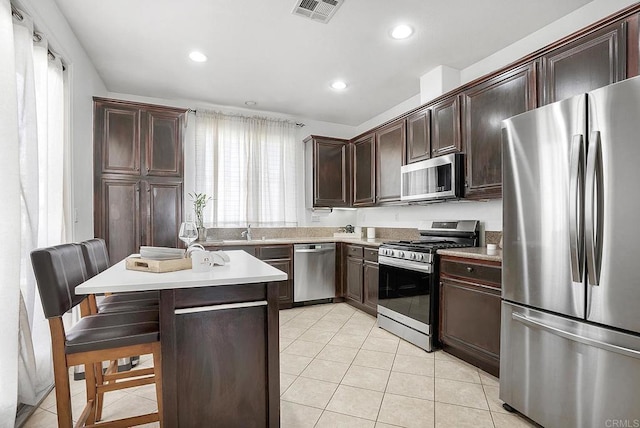 kitchen with dark brown cabinetry, a kitchen bar, light tile patterned floors, a kitchen island, and stainless steel appliances