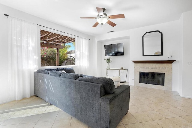 tiled living room with a tiled fireplace and ceiling fan