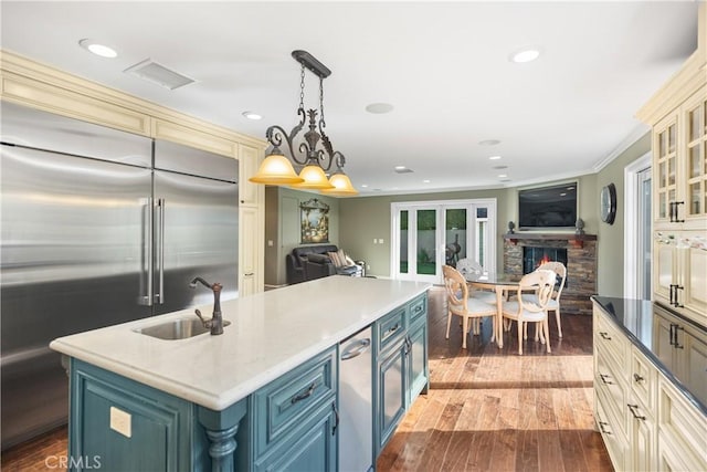 kitchen with a center island with sink, glass insert cabinets, open floor plan, built in refrigerator, and a sink