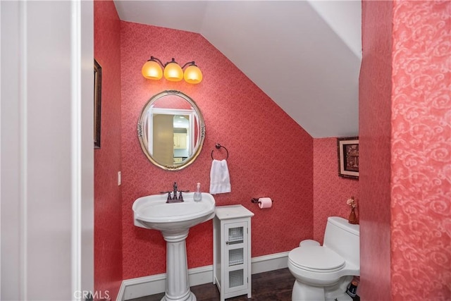 bathroom with toilet, wallpapered walls, baseboards, and vaulted ceiling