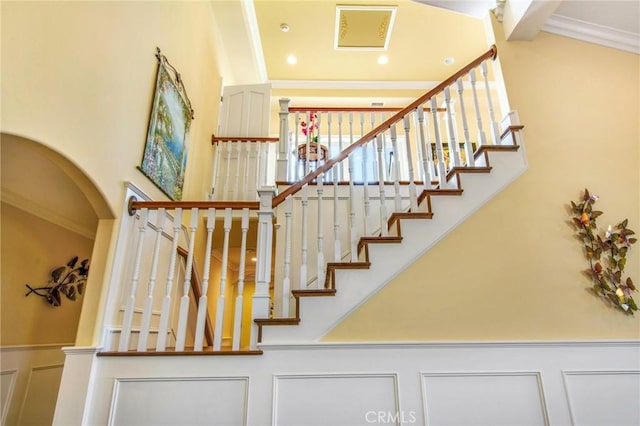 stairs with a wainscoted wall, a high ceiling, a decorative wall, and crown molding