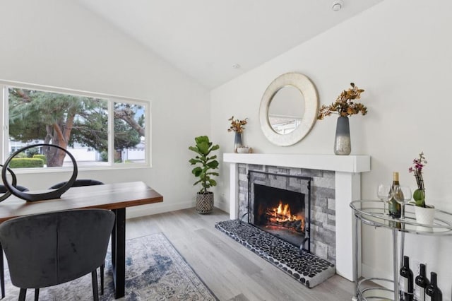 office space with vaulted ceiling, a stone fireplace, and light wood-type flooring