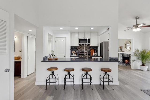 kitchen with appliances with stainless steel finishes, white cabinetry, a kitchen breakfast bar, kitchen peninsula, and light hardwood / wood-style flooring