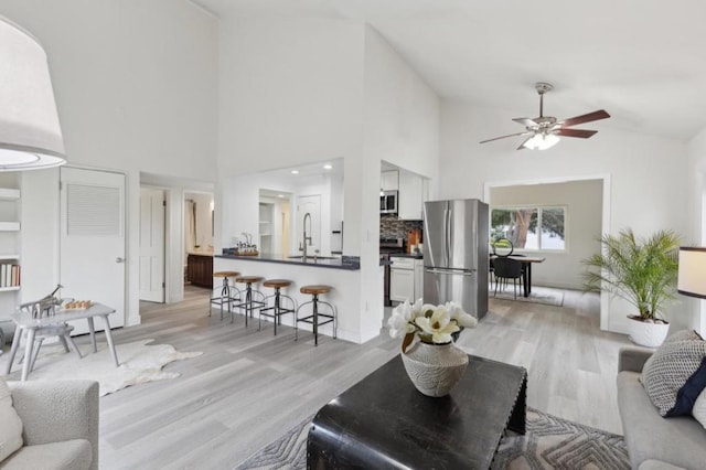 living room with lofted ceiling, sink, light hardwood / wood-style flooring, and ceiling fan