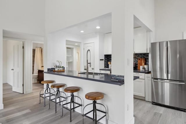 kitchen featuring sink, stainless steel refrigerator, a kitchen breakfast bar, kitchen peninsula, and white cabinets