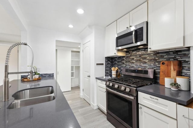 kitchen with appliances with stainless steel finishes, tasteful backsplash, sink, white cabinets, and light wood-type flooring