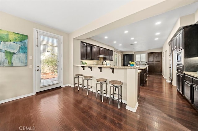 kitchen featuring built in microwave, dark hardwood / wood-style floors, light stone counters, and a kitchen breakfast bar