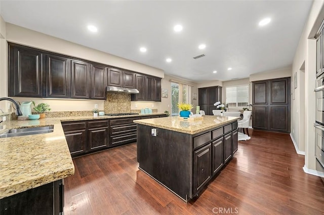 kitchen featuring light stone counters, sink, dark wood-type flooring, and a center island