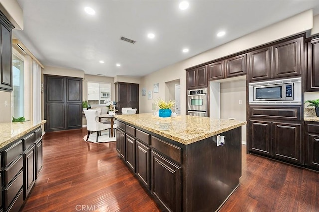 kitchen with stainless steel appliances, a kitchen island, dark wood-type flooring, and light stone counters