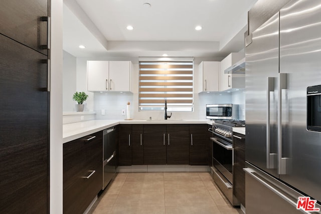 kitchen featuring high end appliances, sink, light tile patterned floors, and white cabinets