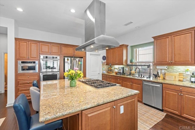 kitchen featuring island exhaust hood, a sink, a kitchen island, appliances with stainless steel finishes, and light stone countertops