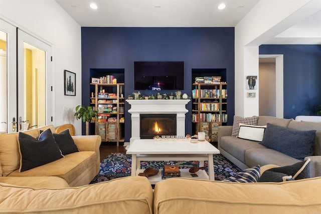 living room with wood finished floors, recessed lighting, a warm lit fireplace, french doors, and an accent wall