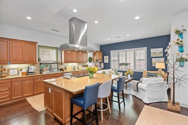 kitchen featuring light stone counters, a kitchen island, dark wood-style floors, a breakfast bar area, and island range hood