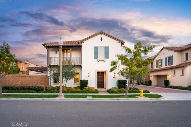 mediterranean / spanish-style home featuring a balcony, fence, stucco siding, a tiled roof, and decorative driveway