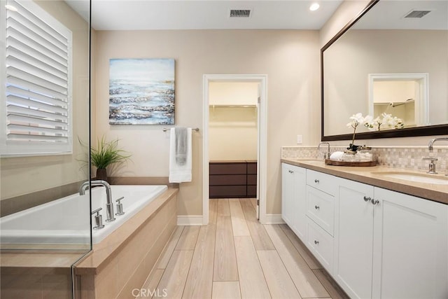 bathroom with hardwood / wood-style flooring, vanity, tiled bath, and backsplash