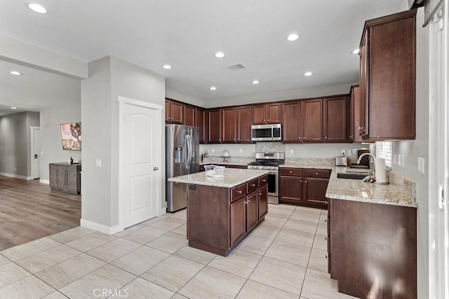 kitchen with appliances with stainless steel finishes, light stone countertops, sink, and a kitchen island