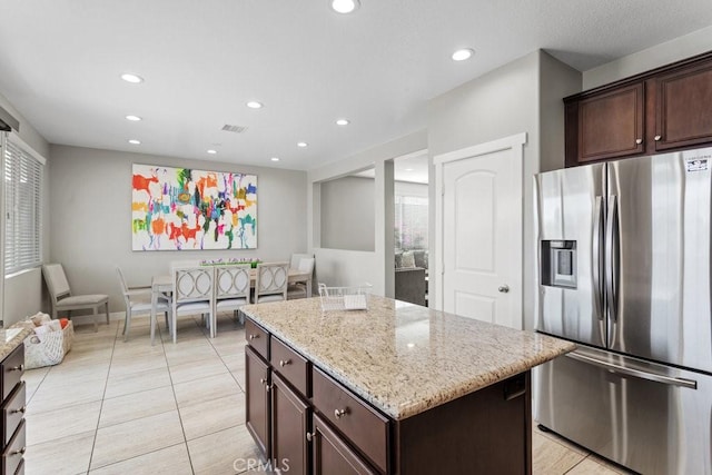 kitchen featuring light tile patterned floors, a center island, stainless steel refrigerator with ice dispenser, light stone counters, and dark brown cabinetry