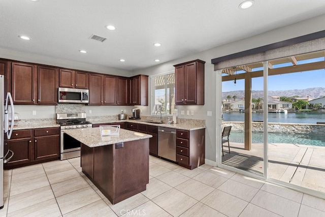 kitchen featuring light tile patterned floors, appliances with stainless steel finishes, a water and mountain view, light stone countertops, and a kitchen island