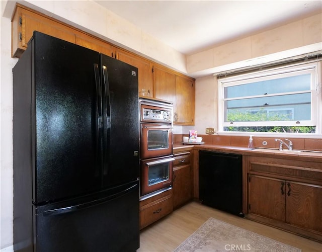 kitchen featuring a sink, black appliances, brown cabinetry, and light wood-style floors