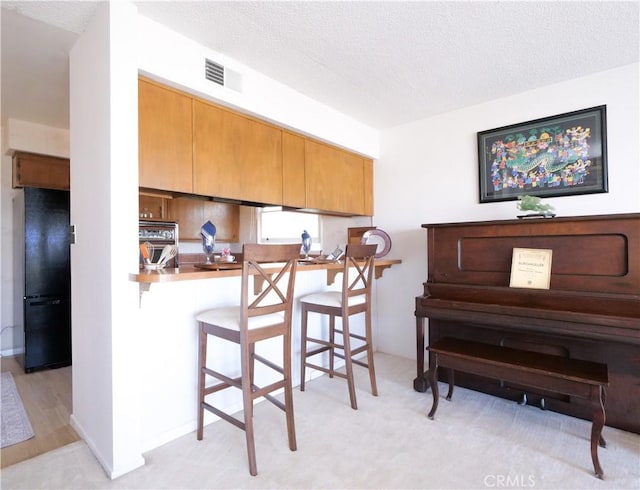 kitchen featuring freestanding refrigerator, a kitchen breakfast bar, a textured ceiling, and visible vents