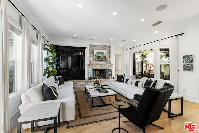 living room featuring ornamental molding, a stone fireplace, and light hardwood / wood-style floors