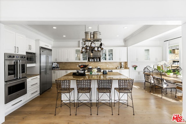 kitchen with white cabinets, a kitchen bar, a center island, stainless steel appliances, and light hardwood / wood-style flooring