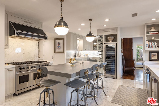 kitchen featuring decorative light fixtures, range hood, beverage cooler, range with two ovens, and a kitchen island with sink