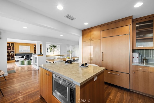 kitchen featuring tasteful backsplash, stainless steel microwave, dark hardwood / wood-style flooring, and a center island