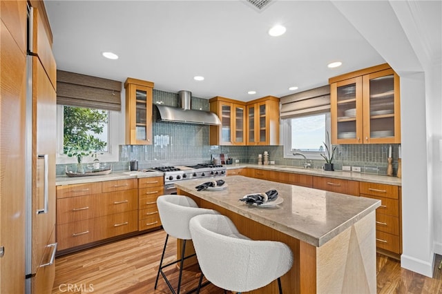 kitchen featuring sink, a breakfast bar area, a center island, light hardwood / wood-style floors, and wall chimney exhaust hood