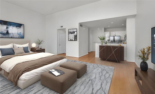 bedroom featuring stainless steel refrigerator, a high ceiling, and light wood-type flooring