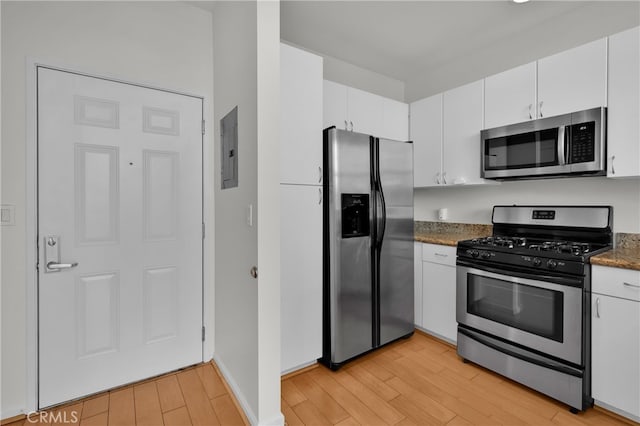 kitchen featuring white cabinets, dark stone counters, electric panel, stainless steel appliances, and light wood-type flooring