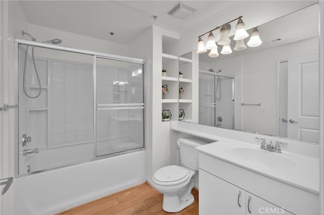 full bathroom featuring wood-type flooring, combined bath / shower with glass door, vanity, and toilet