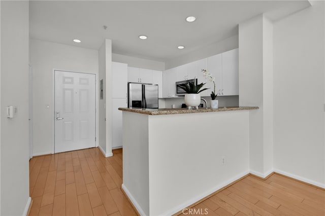 kitchen featuring stainless steel appliances, kitchen peninsula, light hardwood / wood-style flooring, and white cabinets