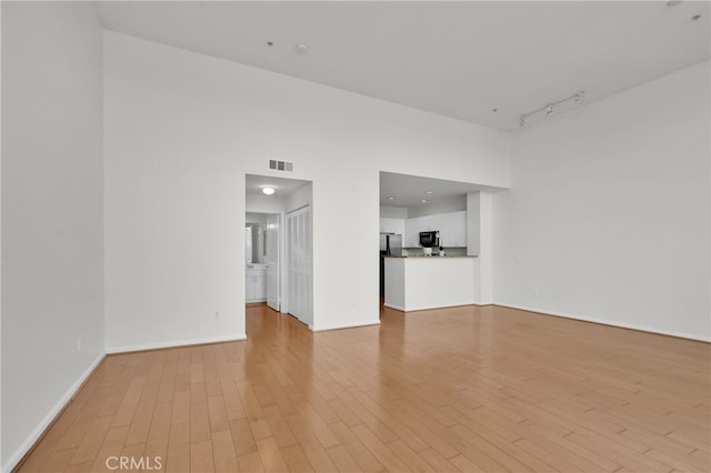 unfurnished living room featuring a high ceiling and light hardwood / wood-style flooring