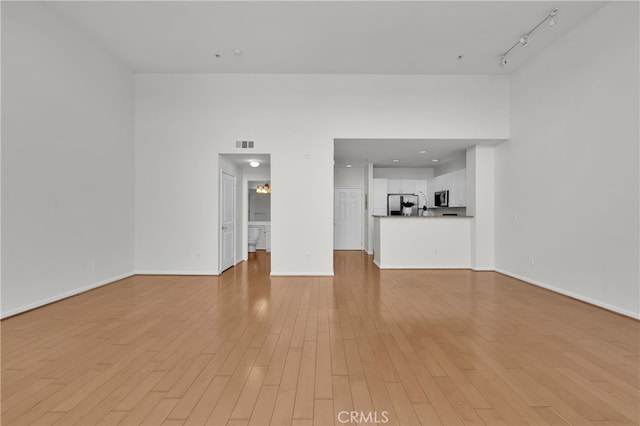 unfurnished living room with rail lighting, a towering ceiling, and light wood-type flooring