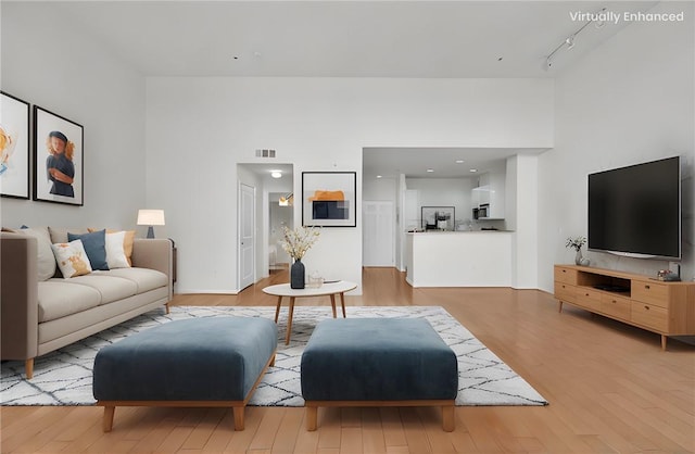 living room with a high ceiling, track lighting, and light wood-type flooring