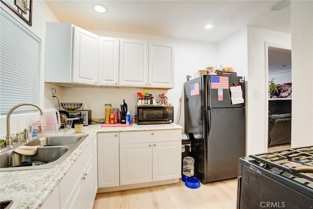 kitchen featuring white cabinetry, sink, gas range, black fridge, and light wood-type flooring