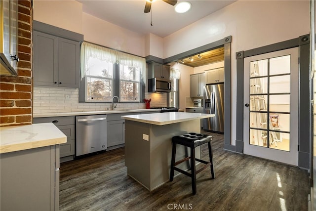 kitchen featuring stainless steel appliances, a kitchen island, gray cabinetry, and a kitchen breakfast bar