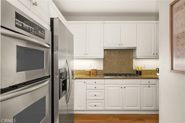 kitchen featuring dark stone countertops, decorative backsplash, white cabinets, and appliances with stainless steel finishes