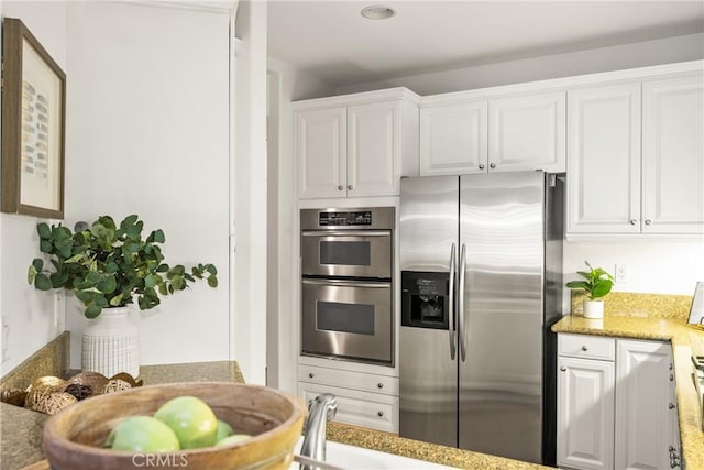 kitchen with stainless steel appliances, light stone countertops, and white cabinets