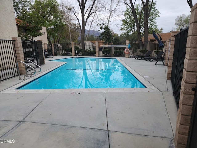 community pool with a mountain view, fence, and a patio