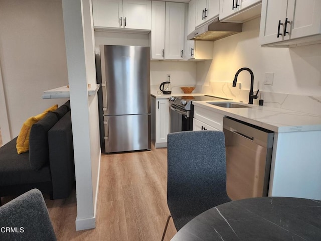 kitchen with appliances with stainless steel finishes, light wood-type flooring, under cabinet range hood, white cabinetry, and a sink