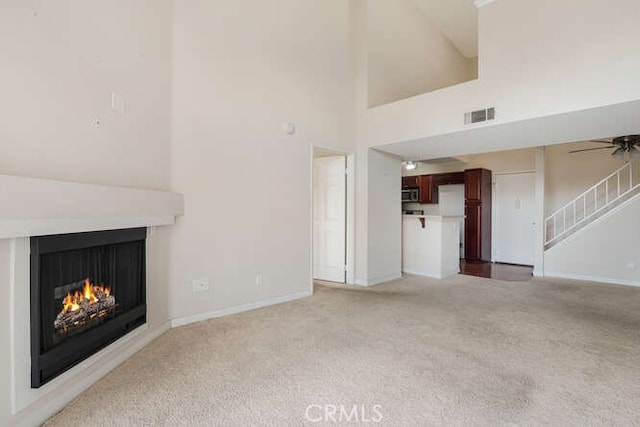 unfurnished living room with light carpet, ceiling fan, and a high ceiling