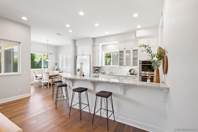 kitchen featuring decorative light fixtures, a kitchen breakfast bar, dark hardwood / wood-style flooring, stainless steel appliances, and white cabinets